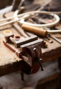 A vintage bench vice on an old workbench in a rustic workshop, showcasing carpentry tools.