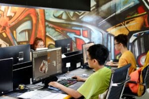 Three young people working on computers in a creative office with vibrant graffiti walls.